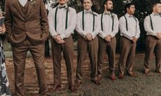 a group of men standing next to each other in front of trees and dirt ground