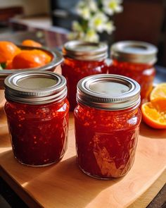 three jars filled with jam sitting on top of a cutting board next to oranges