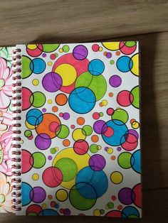 an open spiral notebook with colorful circles and dots on it, sitting on a wooden surface