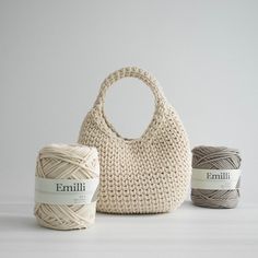 three balls of yarn and a bag on a white table with two skeins of yarn