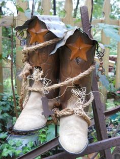 two brown boots are tied up with rope and some other things hanging from the fence