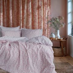 a bed with pink sheets and pillows in front of a window