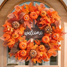 an orange wreath with pumpkins and leaves is hanging on the front door to welcome guests