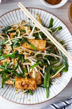 a white plate topped with tofu and veggies next to chopsticks