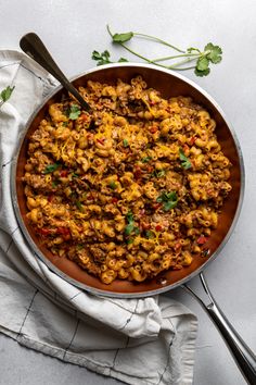 a skillet filled with food on top of a white cloth next to a spoon