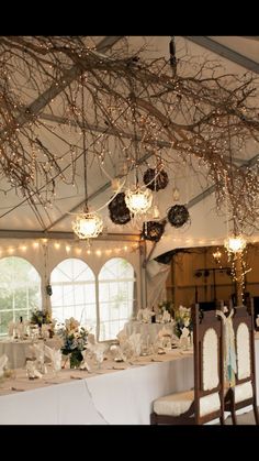 a dining room with tables and chairs covered in white tablecloths, lights and branches