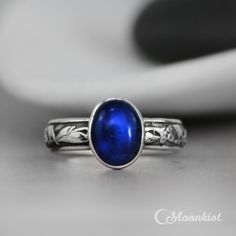 This striking Blue Sapphire Ring features a 10 mm x 8 mm oval cabochon of lab grown Blue Sapphire that has been securely set in a fine silver bezel. Traditionally, people attributed to Blue Sapphire the power to bring harmony between lovers as well as peace between adversaries. We are happy to create this beautiful ring for you in a variety of ring sizes, finish options, or in any of the stone choices shown in the images above. The band of this Sterling Silver ring features an Art Deco inspired Oval Cabochon Sapphire Promise Ring, Classic Oval Blue Moonstone Ring, Sapphire Cabochon Rings For Gifts, Blue Polished Birthstone Ring For Gift, Blue Birthstone Ring With Polished Finish As Gift, Blue Oval Opal Ring With Polished Finish, Blue Sapphire Ring Oval Cabochon, Blue Sapphire Jewelry In Oval Cabochon Shape, Oval Sapphire Moonstone Ring For Anniversary