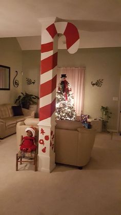 a living room decorated for christmas with a candy cane pole in the corner and a small child sitting on a chair next to it