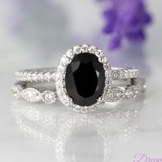 an oval black and white diamond ring on top of a table with purple flowers in the background