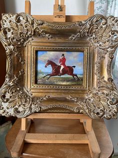 a painting of a man riding a horse in a gold frame on an easel