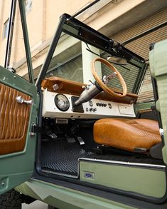 the interior of an old green jeep with leather seat covers and steering wheel, parked in front of a building