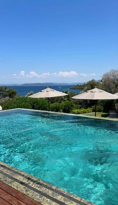 an empty swimming pool surrounded by umbrellas and blue water with the ocean in the background