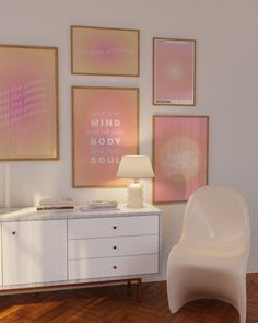 a white chair sitting next to a table with a lamp on it in front of some pictures