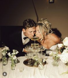 a bride and groom are kissing in front of a table full of wine glasses with flowers