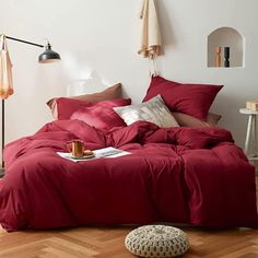 a bed with red comforter and pillows in a room next to a lamp on the wall