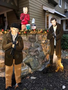 two statues of men standing in front of a stone wall with christmas lights on it