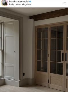 an empty room with large windows and wooden doors on both sides, in front of a white wall