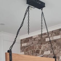 a light fixture hanging from the ceiling in front of a brick wall with chains attached to it