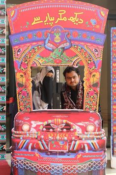 a man and woman standing in front of a colorful vehicle with an intricate design on it