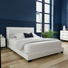 a white bed in a blue room with wooden floors and walls, next to a large window