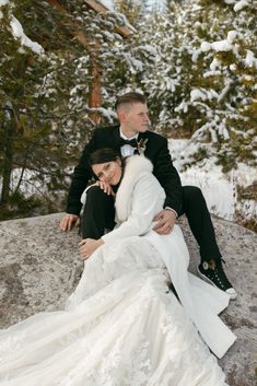 a bride and groom sitting on a rock in the snow