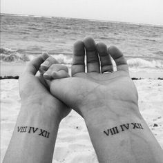 two people are holding hands with roman numerals on their wrists and the ocean in the background