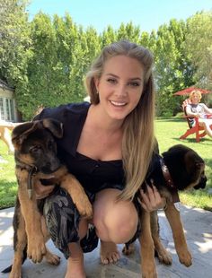 a woman kneeling down with two dogs in her lap and one dog on her lap