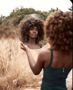 a woman is looking at her reflection in the mirror while she brushes her afro hair