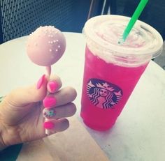 a hand holding a lollipop next to a pink drink