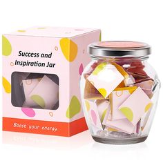 a glass jar filled with pink and yellow paper cubes next to a cardboard box