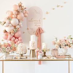 a table topped with lots of cake next to a wall covered in balloons and flowers