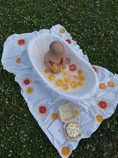 a baby in a bathtub with oranges on the ground next to an open container