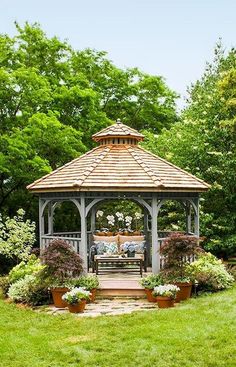 a gazebo in the middle of a grassy area with potted plants and flowers