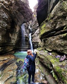 a woman standing in front of a waterfall with her back to the camera and looking up at it