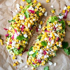 two pieces of bread with corn and feta cheese on top, sitting on wax paper