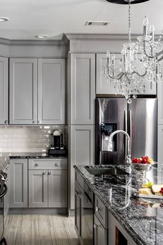 a kitchen with gray cabinets and marble counter tops, chandelier hanging from the ceiling