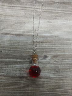 a bottle filled with red liquid sitting on top of a wooden table next to a chain