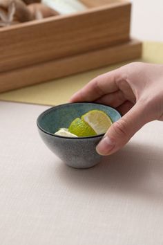 a person holding a lemon slice in a bowl on a table with chopsticks