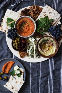 a table topped with plates of food and bowls of dips next to crackers