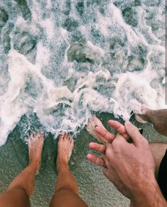 two people sitting on the beach with their feet in the water