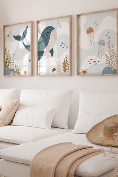 three framed pictures hang on the wall above a white couch in a room with pillows and blankets