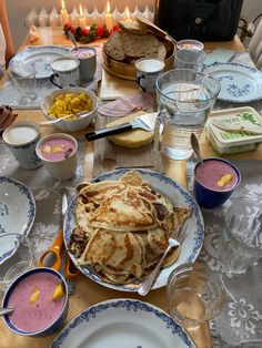 a table topped with lots of plates and bowls filled with food next to candles on top of a wooden table