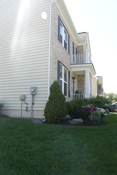 a house that has grass and bushes in front of it, with the sun shining through the windows