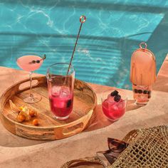 two glasses with drinks sitting on a tray next to a swimming pool