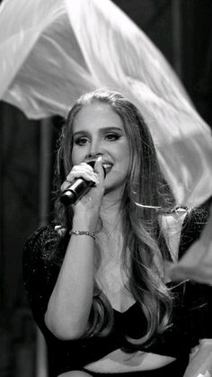 a woman singing into a microphone while holding an umbrella behind her back to the camera