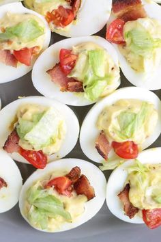 deviled eggs filled with bacon, lettuce and tomato on a white plate