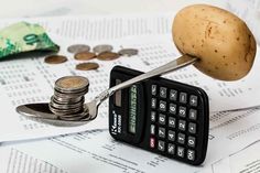 a calculator with a potato on top of it next to some coins and a spoon