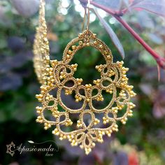 a gold necklace hanging from a tree branch with beads and leaves in the foreground