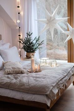 a bed with white sheets and pillows next to a christmas tree in front of a window