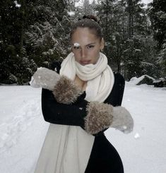 a woman standing in the snow with her arms crossed wearing gloves and a scarf around her neck